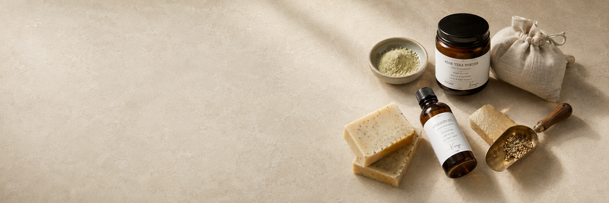 Aloe vera powder, avocado oil, handmade soap bars and a brass scoop on a sunlit stone surface